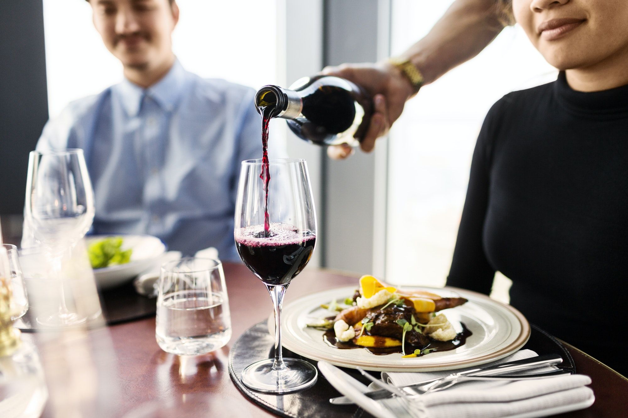 Cropped image of waiter serving red wine for female customer at restaurant